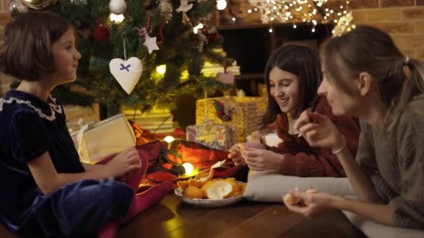 Mamá y dos hijas pasando un buen rato juntas, comiendo mandarinas bajo el árbol de Navidad en casa — Vídeos de Stock