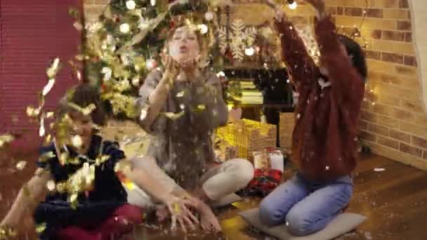 Η μαμά και οι κόρες πιάνουν χρωματιστά κομφετί στο χέρι χαρούμενα γελώντας κοντά στο χριστουγεννιάτικο δέντρο — Αρχείο Βίντεο