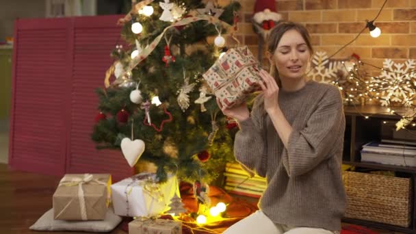 Blonde Frau schüttelt Weihnachtsgeschenkschachtel und erraten, was drin ist — Stockvideo