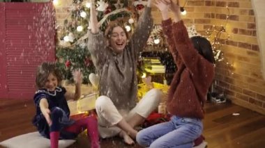 Anne ve kızları gülüp eğleniyorlar, evde beyaz konfeti atıyorlar.