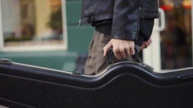 Gitar çantasıyla sokakta yürüyen bir adam.