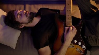 Kanepede gözleri kapalı uzanan bir adam gitar çalıyor.