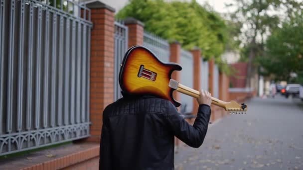 Man går ner på gatan med en gitarr på axeln — Stockvideo