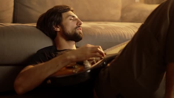 Man playing on guitar while sitting on the floor in smoked room with closed eyes — Stock Video