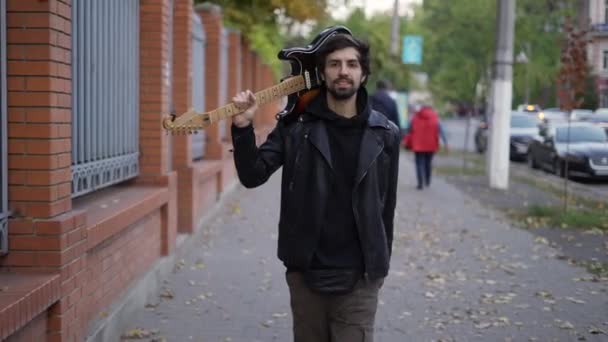Счастливчик идет по улице с гитарой на плече — стоковое видео