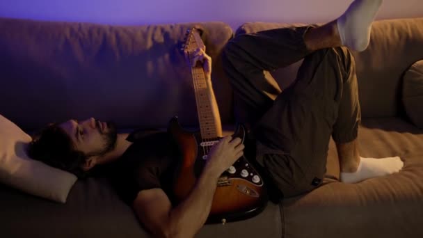 Man composing music on guitar while lying on sofa — Stock Video