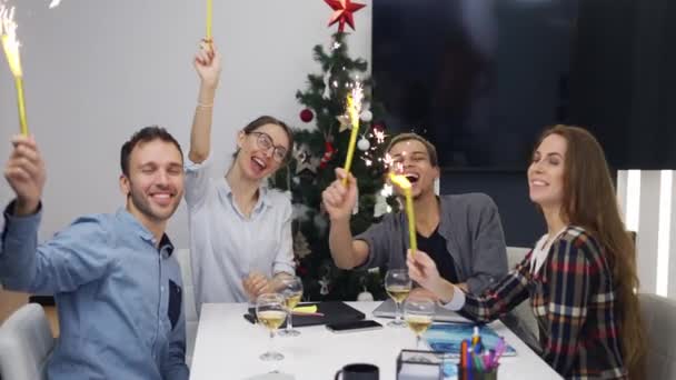 Podekscytowani koledzy z biura świętują świąteczne przyjęcie firmowe, wymachując złotymi iskrami — Wideo stockowe