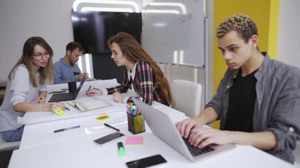 Молодые креативные бизнесмены общаются, работают с ноутбуками в офисе — стоковое видео