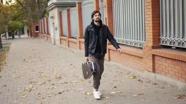 Elinde gitar çantası olan bir adam caddede yürüyor. — Stok video