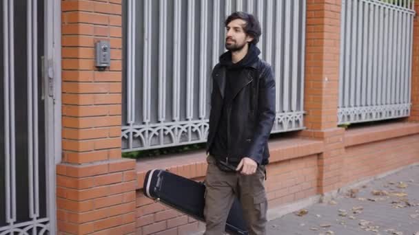 Homem feliz segurando uma caixa de guitarra enquanto caminha — Vídeo de Stock