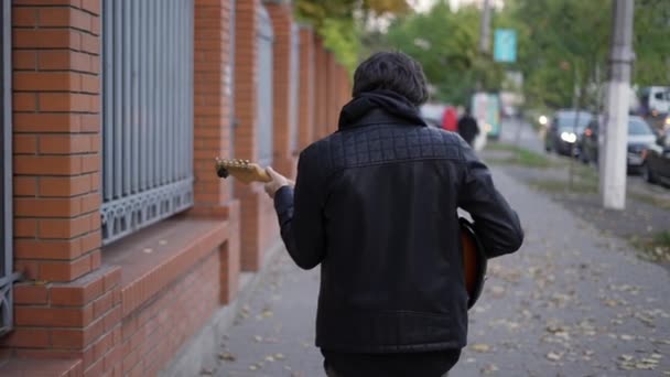 Egy férfi sétál az utcán és gitározik. — Stock videók