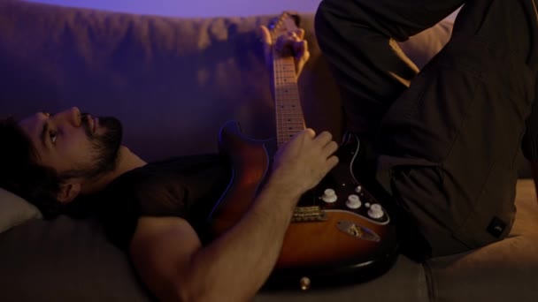 インスピレーションを受けた男はソファに横たわっながらギターで音楽を作曲 — ストック動画