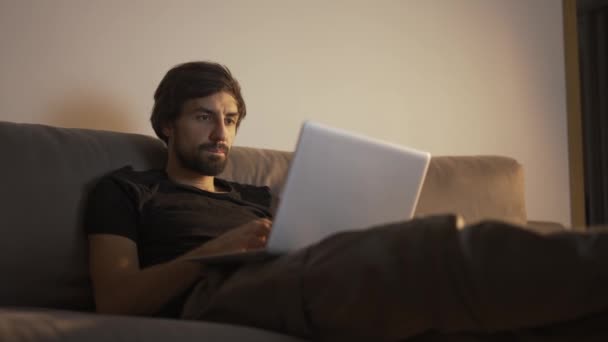 Hombre concentrado trabajando en un portátil en casa mientras está sentado en el sofá — Vídeos de Stock