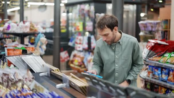 Mann läuft durch Supermarkt und holt Schokolade aus dem Regal Etiketten und Zutaten lesen — Stockvideo