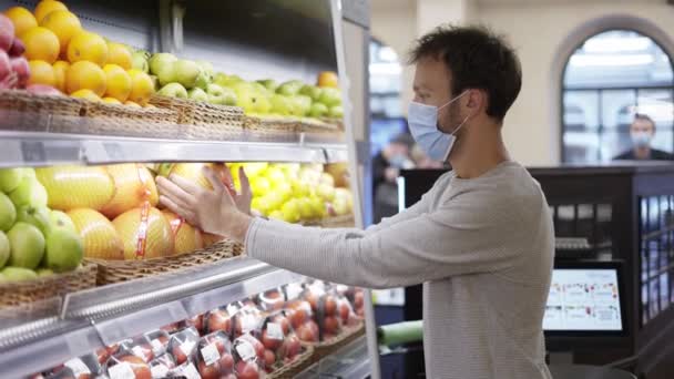 El hombre enmascarado toma un cítrico fresco de la estantería de alimentos. Comprador elegir pummelo en la tienda de comestibles — Vídeos de Stock