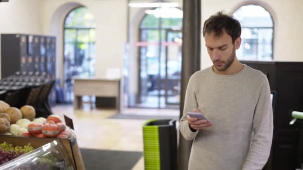 Hombre relajado caminando por la tienda mirando la pantalla de su teléfono inteligente — Vídeos de Stock