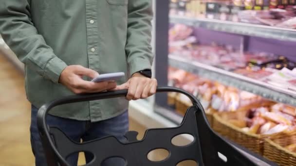 Hombre usando el teléfono móvil mientras que hace compras en el supermercado, tienda de comestibles del centro comercial del carro — Vídeo de stock