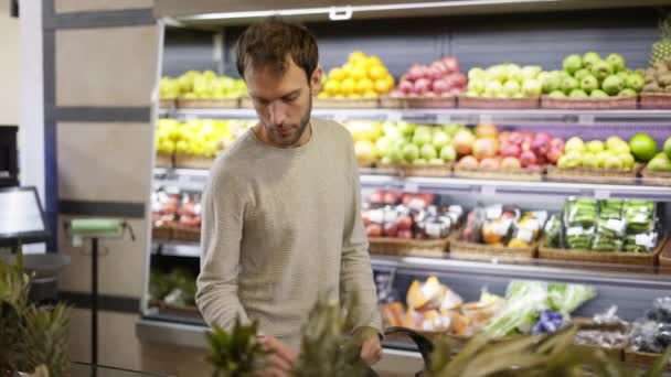 男は食べ物棚から新鮮な果物を取る。食料品店で柿を選ぶ買い物客 — ストック動画