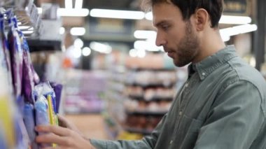 Gergin adam alışveriş yapıyor. Raftan paketi almaya çalışan sinirli bir adam. Süpermarkette müşterilerin üzerine düşen mallar