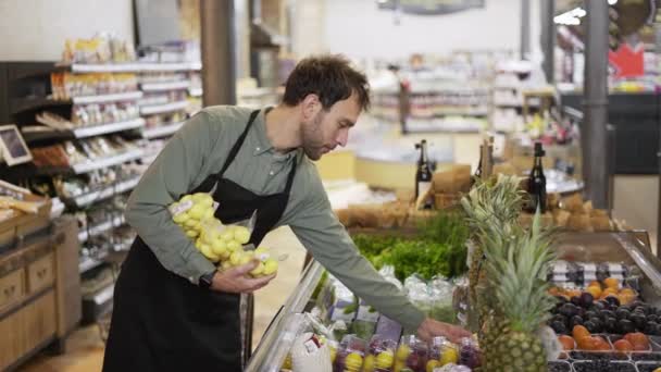 Mitarbeiter eines Lebensmittelgeschäfts kaukasischer Bärtiger arrangiert verpackte Kartoffeln in Schürze im modernen Bio-Supermarkt Lebensmittelladen — Stockvideo