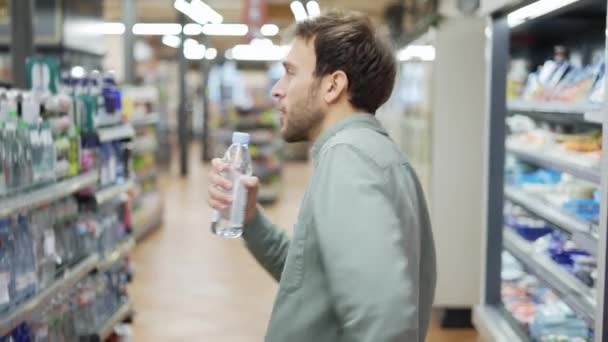 Mann im Supermarkt tanzt und singt Lippenstift. Mit einer Flasche Wasser als Mikrofon. Positive Tänze in einem leeren Lebensmittelladen