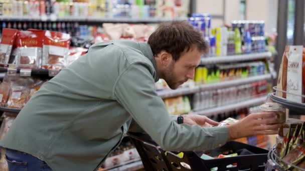 Genç adam süpermarkette kurabiye seçiyor. Markaları, fiyatları, etiketleri ve malzemeleri karşılaştırıyor. Kapat. — Stok video