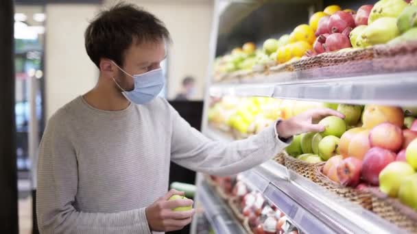 El hombre con máscara toma una manzana fresca de la estantería de alimentos. Comprador elegir manzana en la tienda de comestibles — Vídeos de Stock