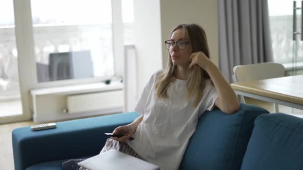 Mladá žena sedící na pohovce s dálkovým ovládáním v rukou a přepínajícími kanály — Stock video