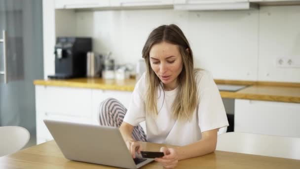 Blonde Frau macht Online-Zahlung mit Bankkarte mit modernem Laptop zu Hause — Stockvideo