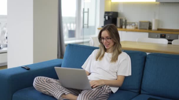 Femme blonde faire appel vidéo chat en ligne regarder l'écran d'ordinateur portable assis sur le canapé — Video