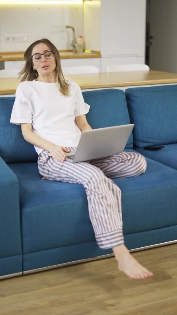 Blondýny žena v pyžamu sedět na gauči a otevírá stříbrný notebook — Stock video