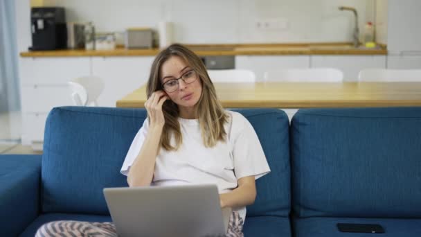 Femme blonde avec ordinateur portable sur les genoux insérant ses écouteurs — Video