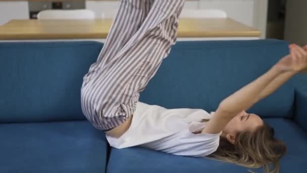 Verspielte blonde Frau im Pyjama zu Hause hat Spaß, tobt auf einer Couch — Stockvideo