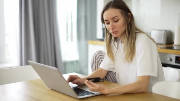 Chica bonita está haciendo el pago en línea de la celebración de la tarjeta bancaria utilizando un portátil moderno en casa — Vídeos de Stock