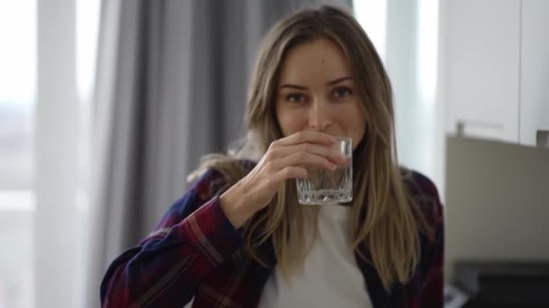 Mujer bebiendo agua en la cocina doméstica, mirando a la cámara — Vídeo de stock