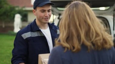 Woman meets a handsome friendly delivery man who gives her a parcel box beside her home. Concept of courier, home delivery, online shopping