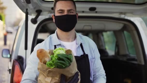 A movement shot of a delivery man wearing protective face mask carrying groceries standing outdoors on the street. Corona virus or COVID 19 epidemic or pandemic — Stok video