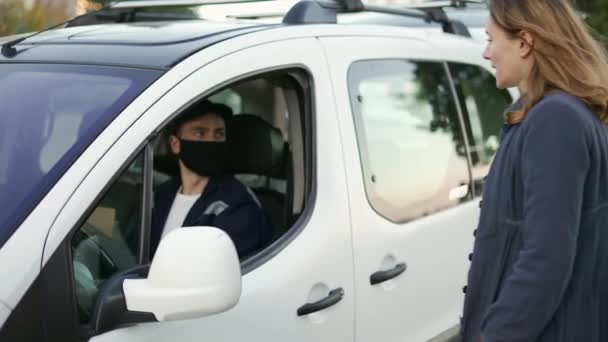 Ο διανομέας που φοράει στολή, μάσκα προστασίας και γάντια παραδίδει ένα πακέτο στον πελάτη του φορτηγού. Χαρούμενη χαμογελαστή γυναίκα που παίρνει το δέμα της από το παράθυρο του αυτοκινήτου. Αργή κίνηση — Αρχείο Βίντεο