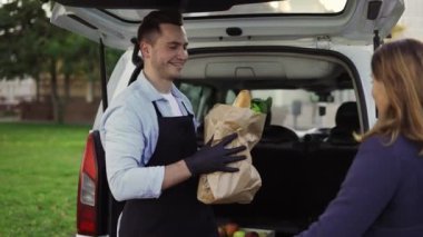 Female customer is getting paper bag of organic groceries from smiling friendly male courier