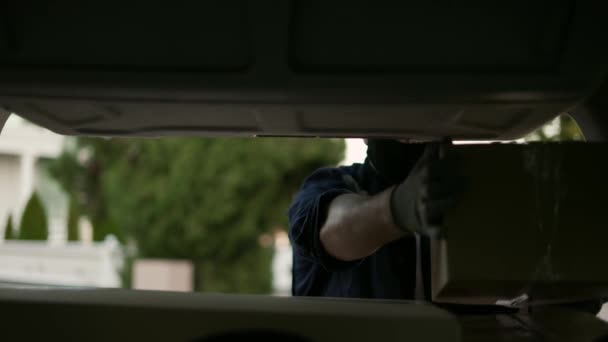 Servicio de entrega. Entrega hombre en una máscara protectora y guantes cerca de un coche poniendo caja de cartón en el maletero. Hombre cerrando minivan tronco con paquetes — Vídeo de stock