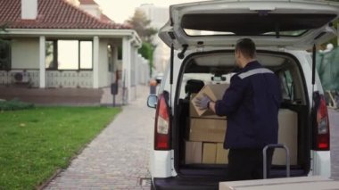 Young handsome Caucasian delivery man putting boxes in van delivering shipment. Male post office worker Courier concept