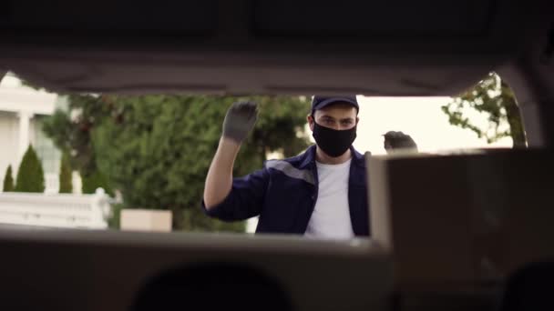 Delivery service. Delivery man in a protective mask and gloves opening the trunk and taking cardboard box parcel. Man closing minivan trunk with parcels. Footage from the backseat of the car — 图库视频影像