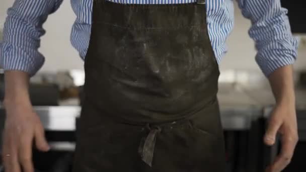 Чоловік пекар витирає руки на фартуху з борошна і кладе руки на стегна — стокове відео