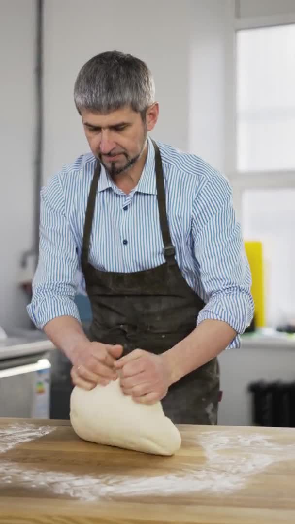 黒エプロン混練生地のハンサムな男性のパン屋さん,パン屋のキッチンでパンを作る.垂直方向の映像 — ストック動画