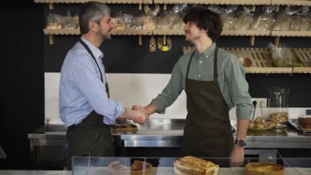 Close up portrait of happy successful family business owners handshaking in their bakery store looking at camera and smiling. Father and son — ストック動画