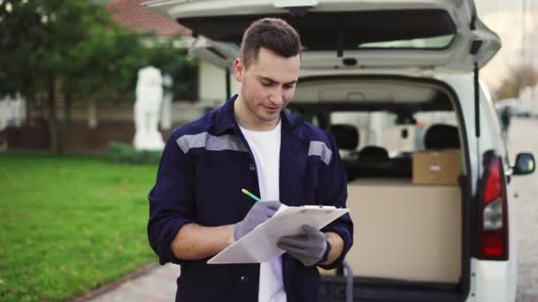 Delivery service worker makes notes on documents and standing on the street near the minivan — 비디오