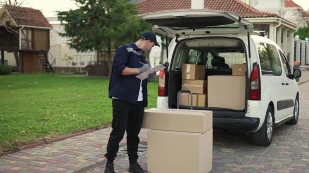 Young delivery man checking list. Delivery man in cap and documentation in hands. Courier with parcel. Male beautiful courier checks the parcels against the delivery list — Video