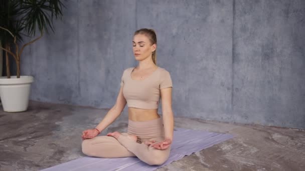 Young female yoga coath sitting in Lotus Pose or Padmasana with closed eyes and holding her hands in Gyan Mudra — Stockvideo