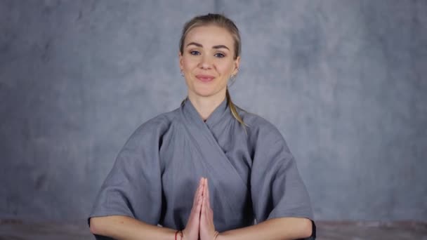 Усміхнена тренерка йога в халаті робить жест Намаса руками — стокове відео
