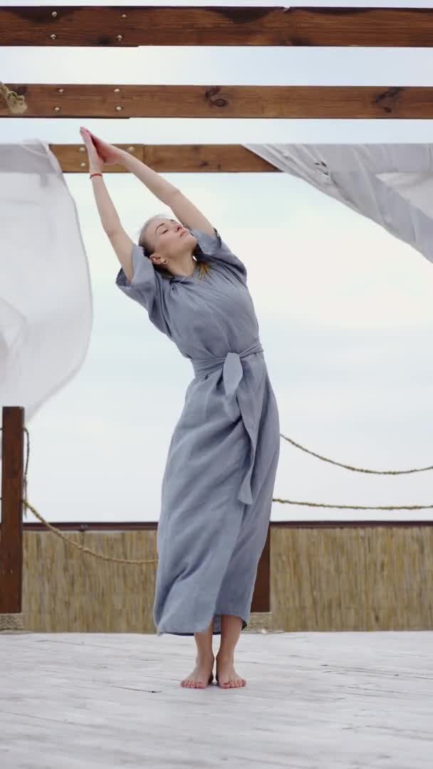 Young blonde woman in the blue robe doing yoga pose at terrace — Vídeo de Stock